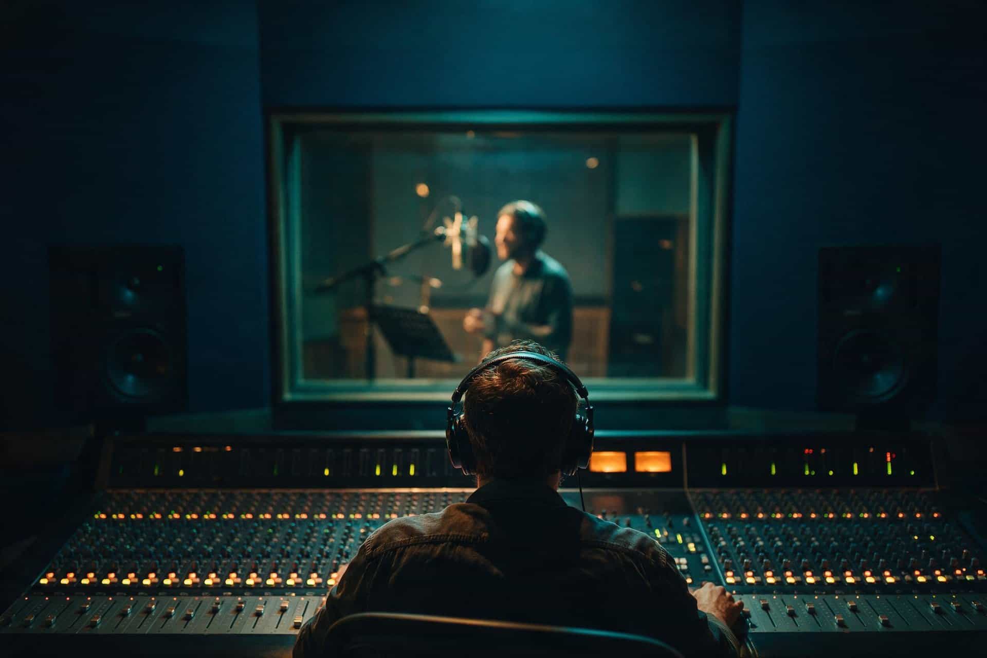 Sound engineer at a mixing desk with a Croatian voice actor recording beyond the studio glass