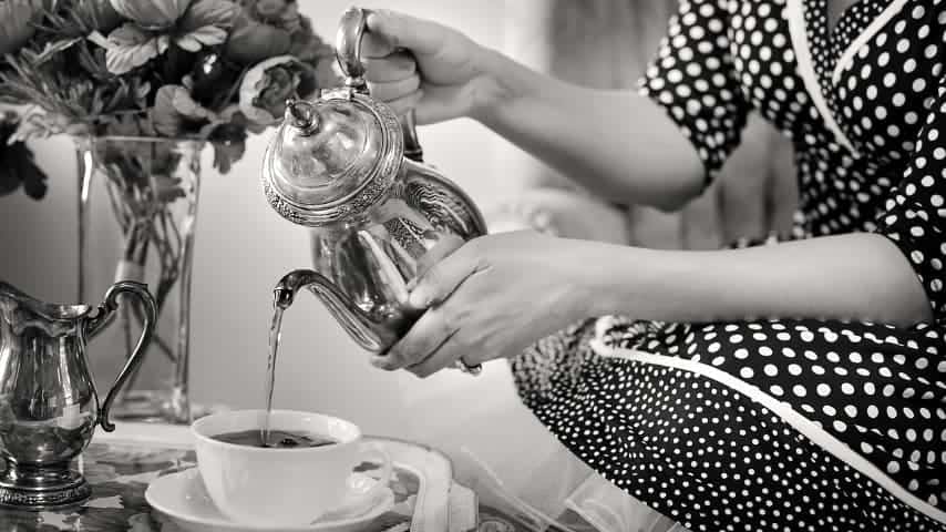 Black and white photo of a woman pouring tea into a teacup