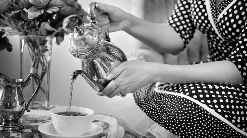 Black and white photo of a woman pouring tea into a teacup