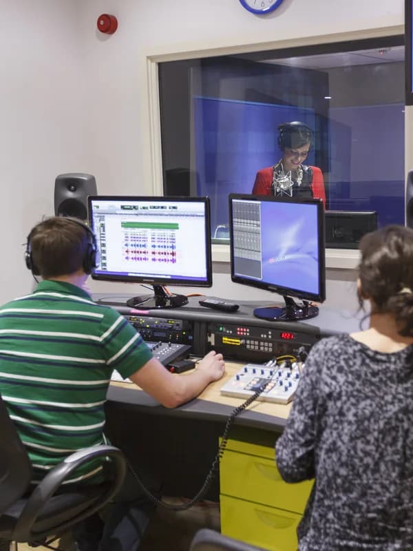 Sound engineer running a session at the desk, booth visible through the glass
