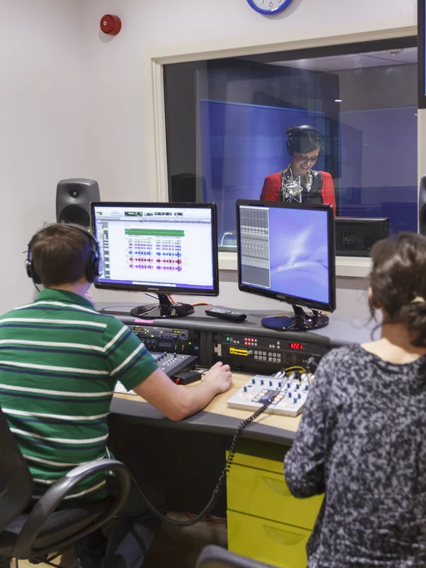 Sound engineer running a session at the desk, booth visible through the glass